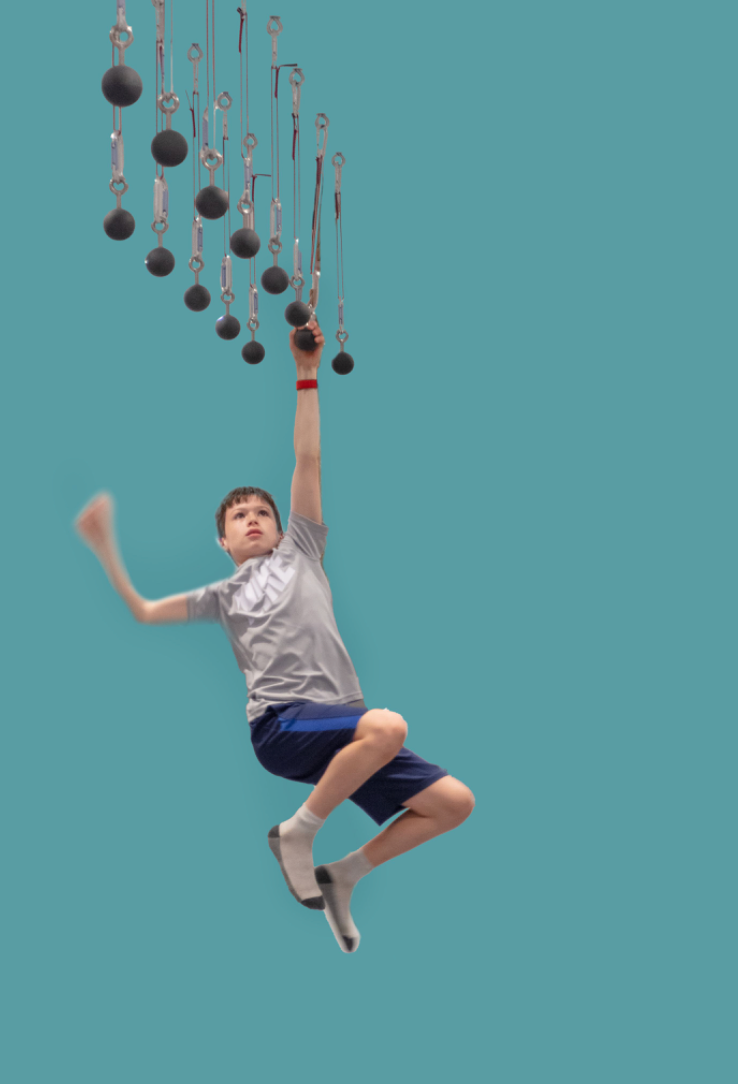Ninja playroom equipment featuring a child joyfully hanging from rings, promoting strength and coordination
