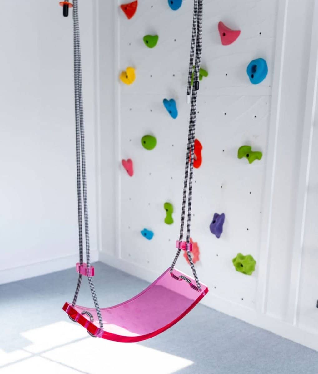 Gabriela designer scoop swing for playroom with a pink seat and climbing wall in the background