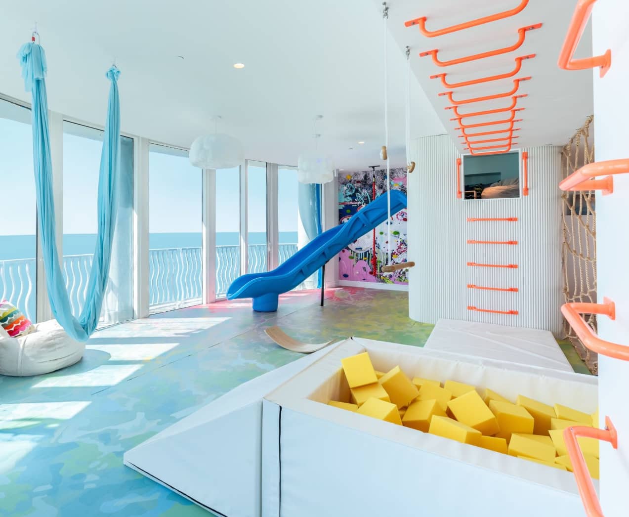 Bright playroom with slide and foam pit for kids filled with yellow foam blocks for safe jumping