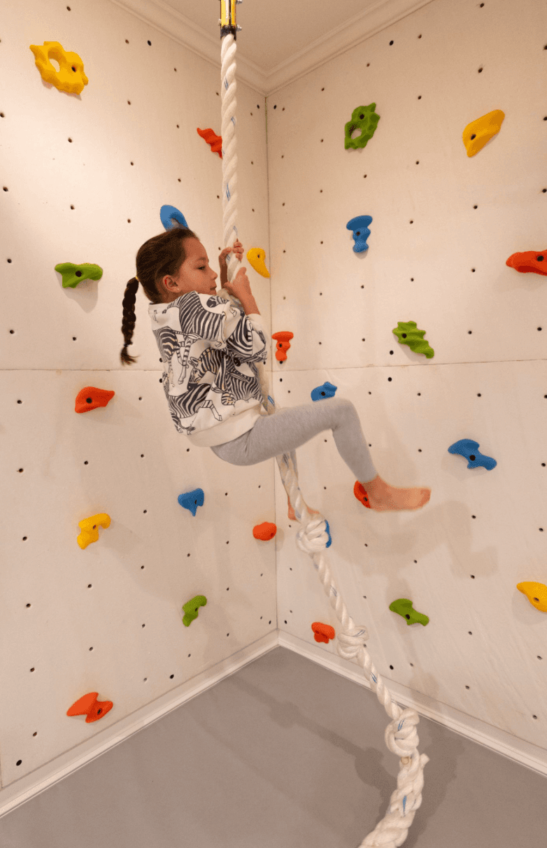 Child climbing on indoor climbing rope for kids in a colorful rock wall playground
