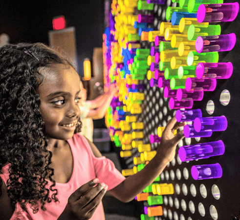 Child using the Lite-Brite peg set for kids on a large colorful display wall