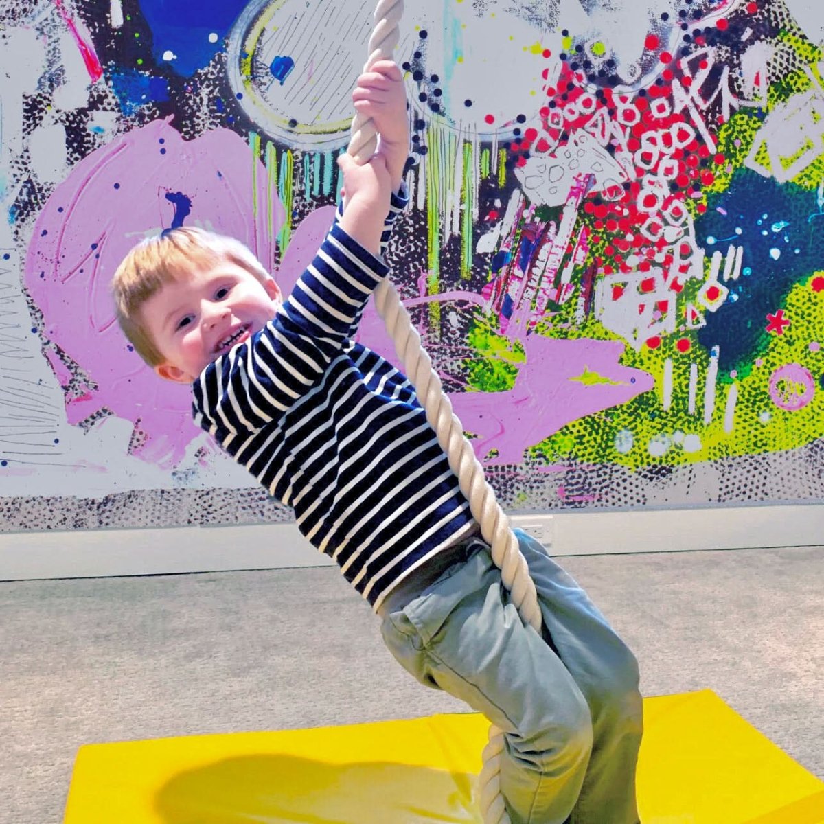 Child swinging on a Jammar indoor climbing rope for kids, set against a colorful wall backdrop
